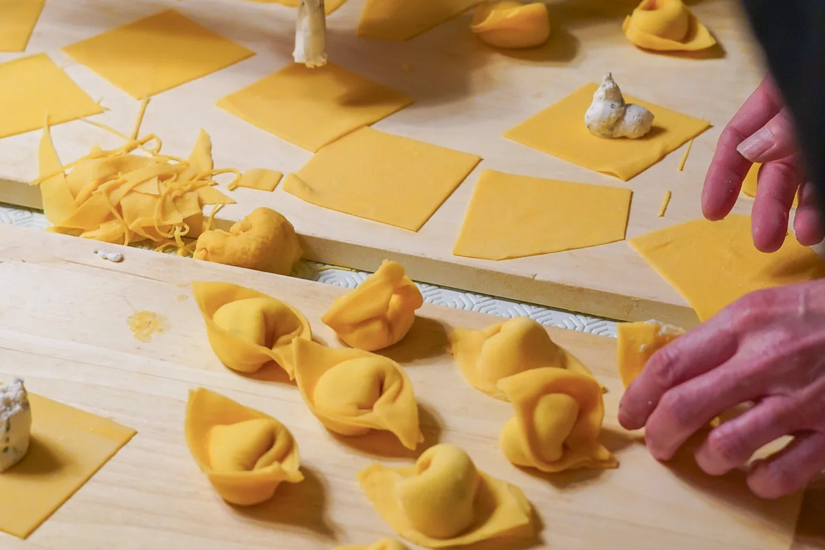 Tortellini chiusi a mano sulla spianatoia, con i quadrati di sfoglia e il ripieno