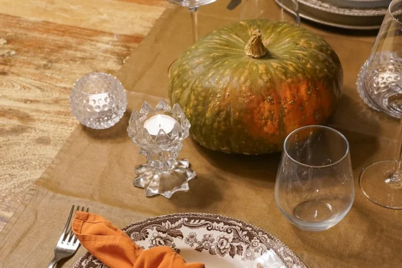An autumn table set with a pumpkin, candles and an orange napkin on the plate